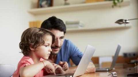 A young boy using a laptop with a male adult watching and helping.