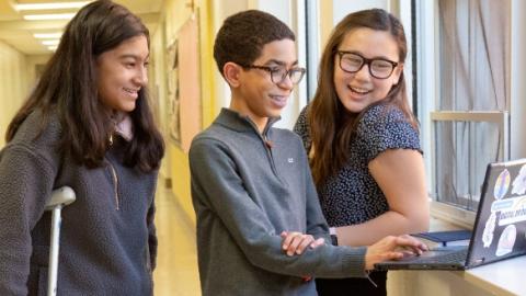 Three tweens using a laptop together.