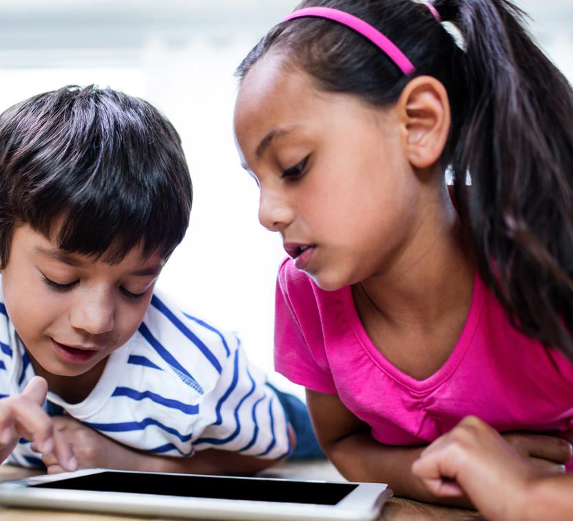 A girl and boy with brown skin look down at a tablet. The boy is scrolling with a finger.